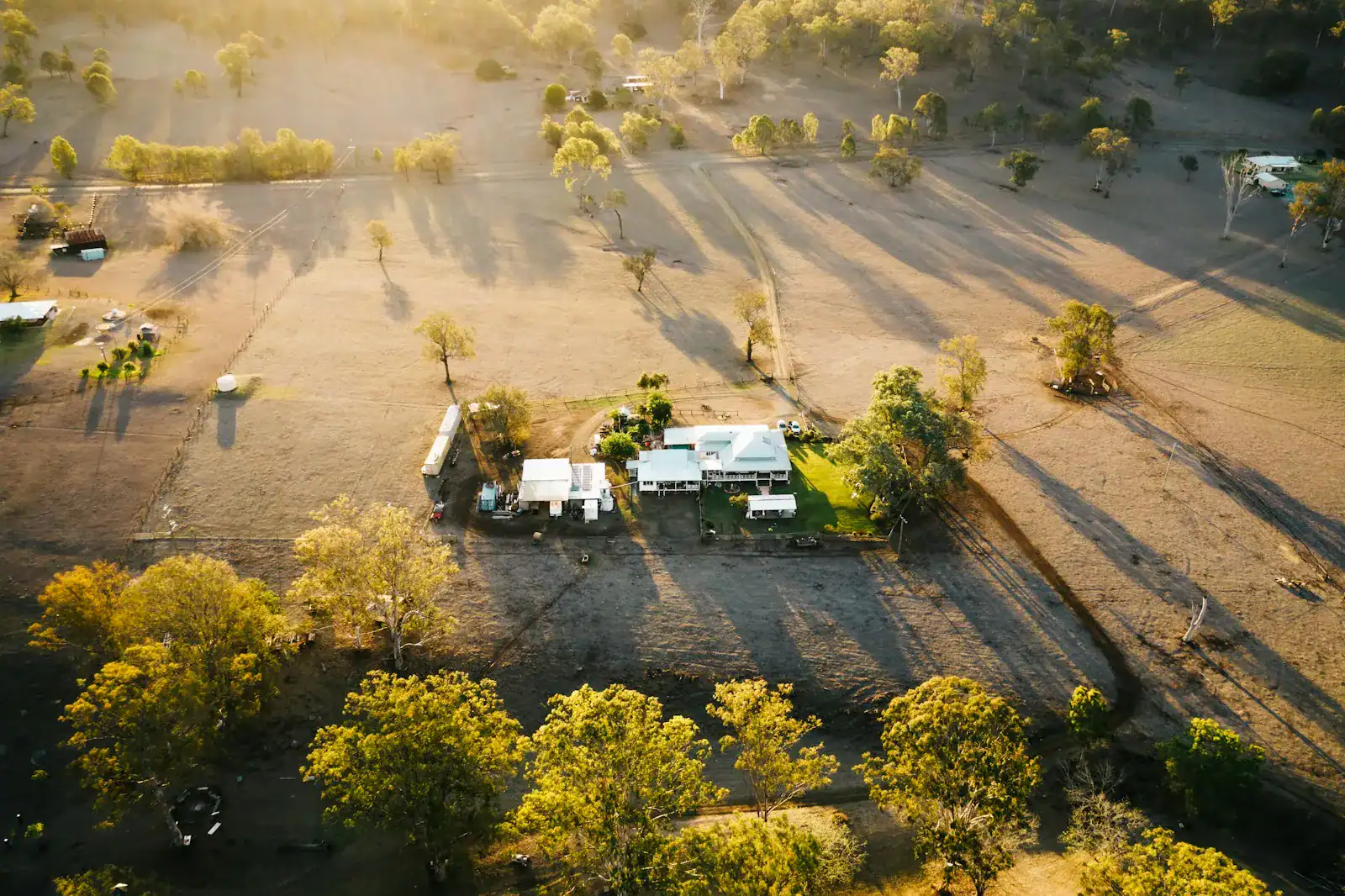 A rural homestead surrounded by paddocks and trees in warm afternoon light