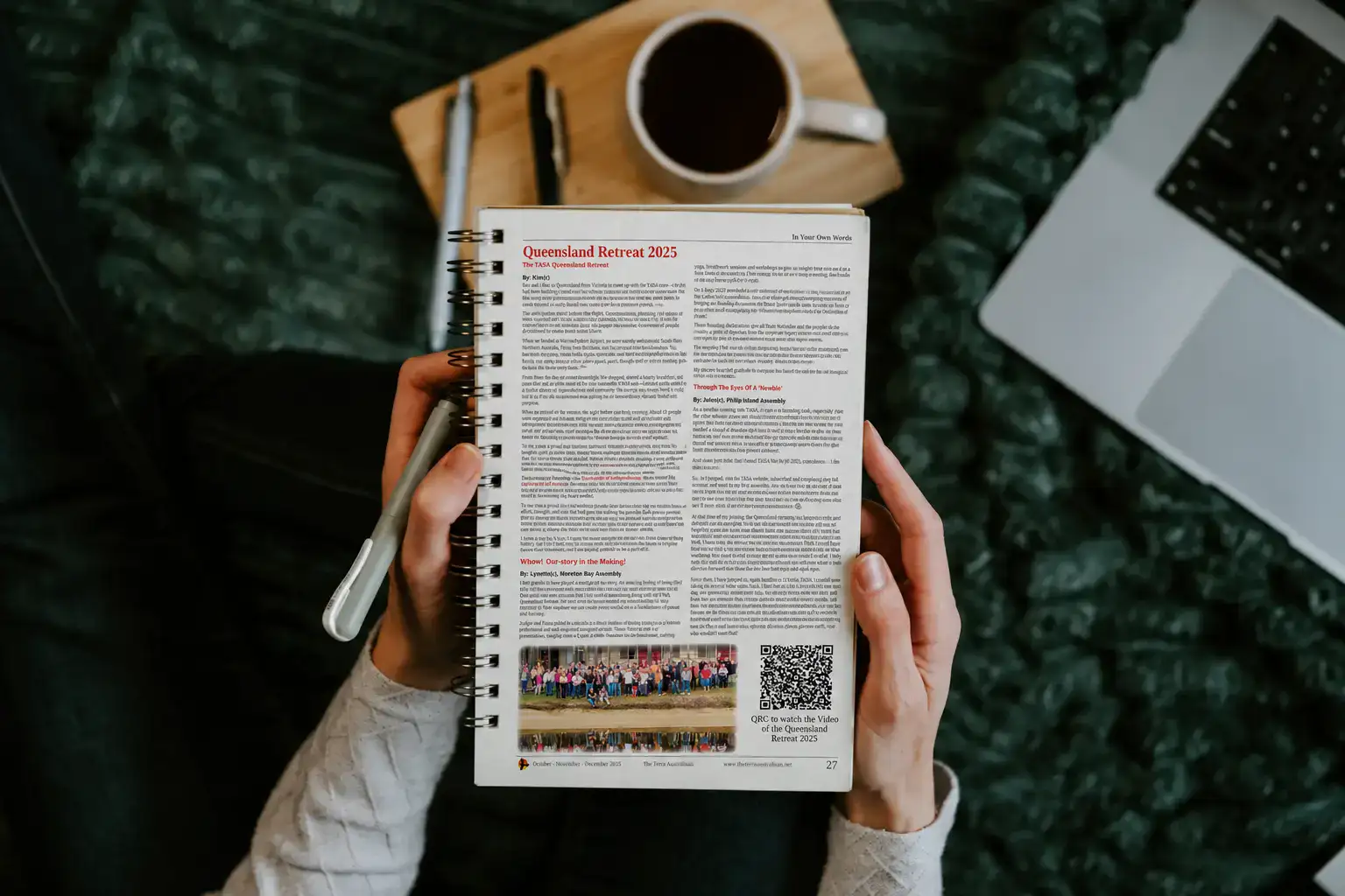 An open book displaying the Queensland Retreat 2025 page from The Terra Australisan beside a coffee and laptop
